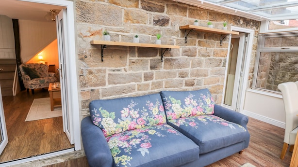 A cozy living room with a stone wall, a blue sofa with floral cushions, and a wooden coffee table. - Willow Nook (Whitby)