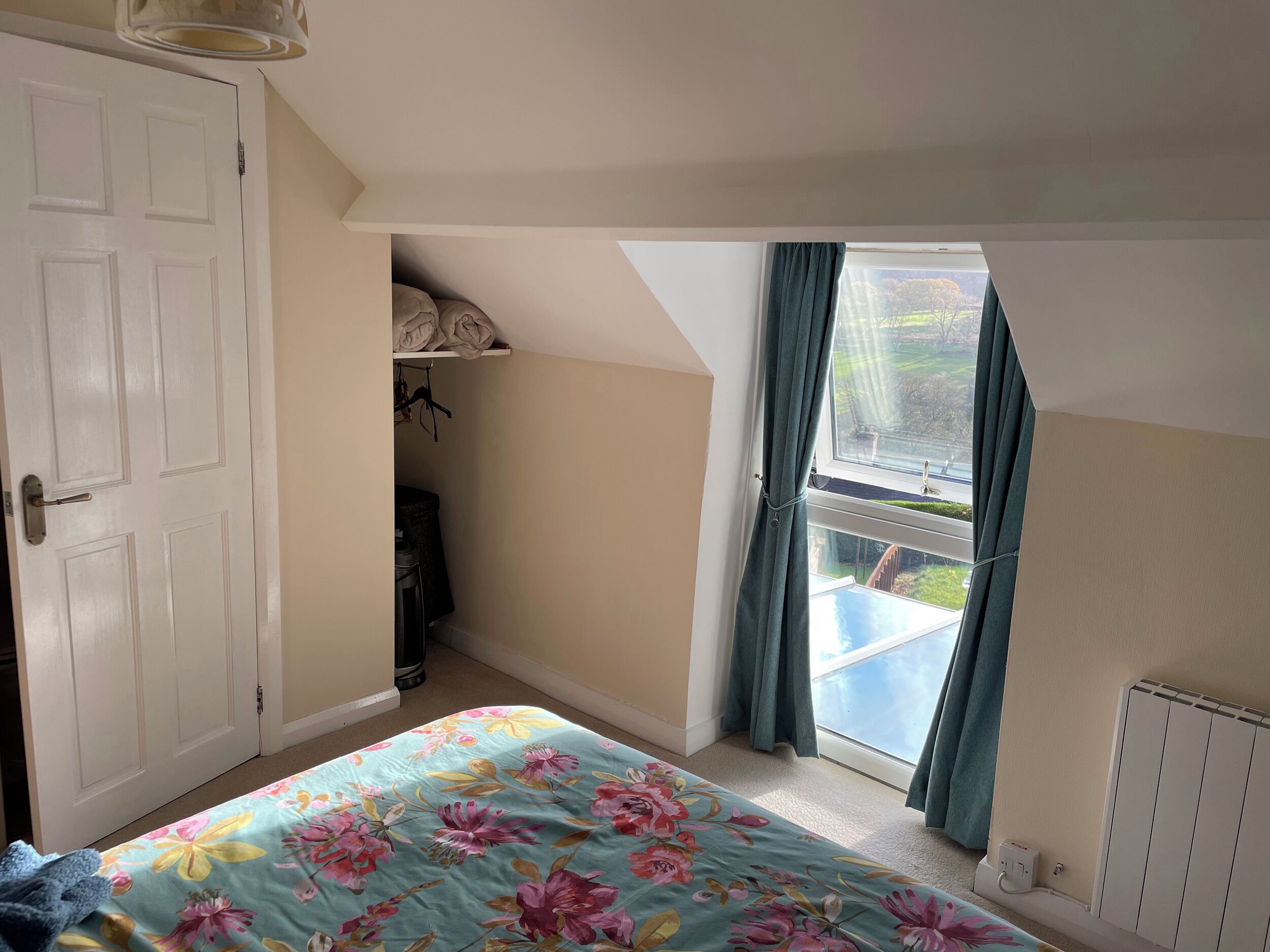 A bedroom with a bed, a wardrobe, a radiator, and a window with curtains.