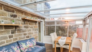 A cozy room with a stone wall, a blue floral sofa, a wooden dining table with chairs, and a glass ceiling. - Willow Nook (Whitby)