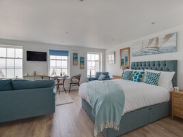 Un espacioso dormitorio con una cama grande, un escritorio con silla, un sofá y vistas al mar a través de las ventanas.