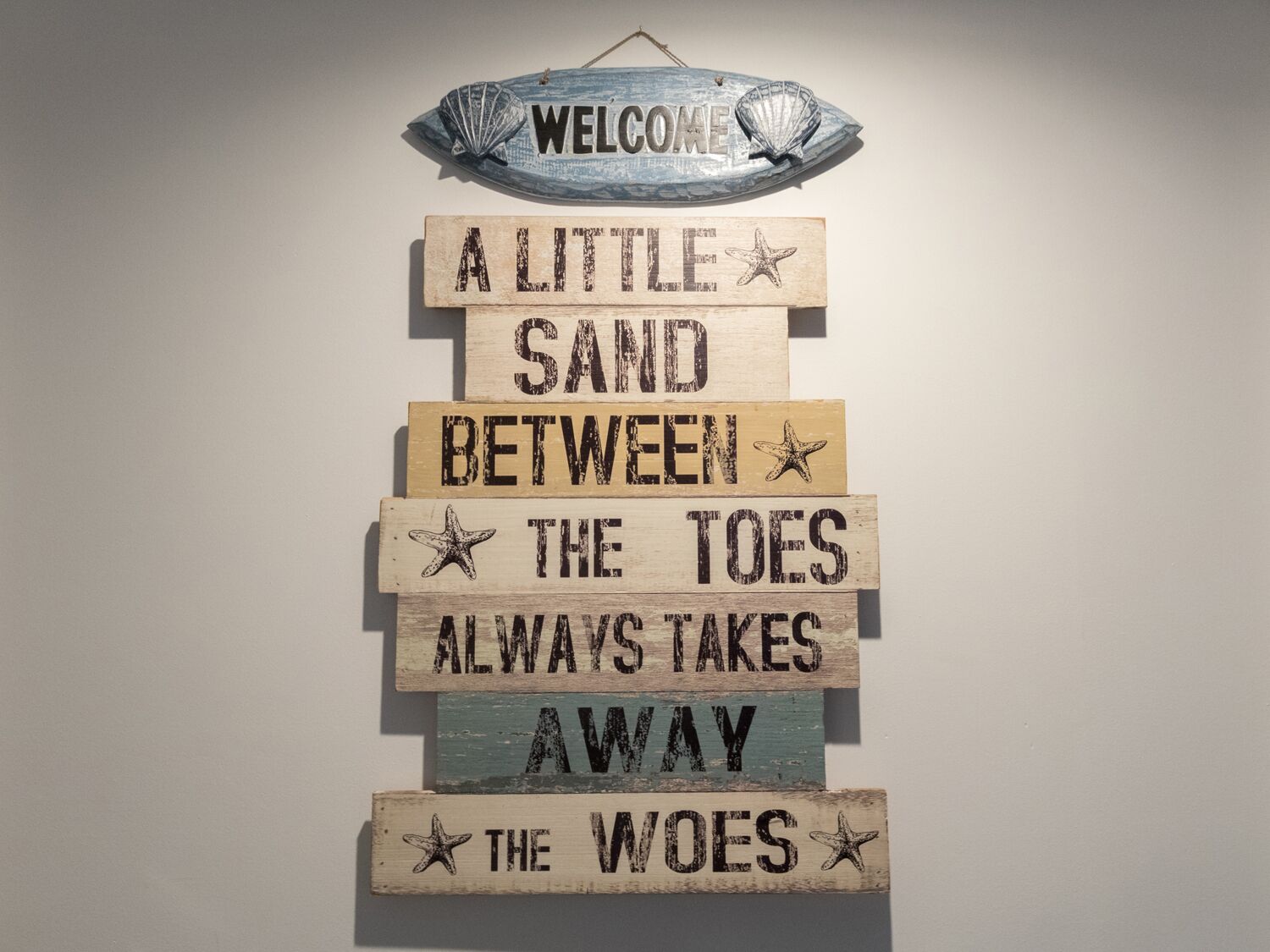 Une plaque en bois fixée au mur, portant l’inscription : « Un peu de sable entre les orteils, et tous les soucis s’envolent. »