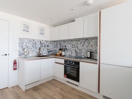 Una cocina compacta con armarios blancos, un salpicadero estampado, horno empotrado y una pequeña encimera con diversos objetos.