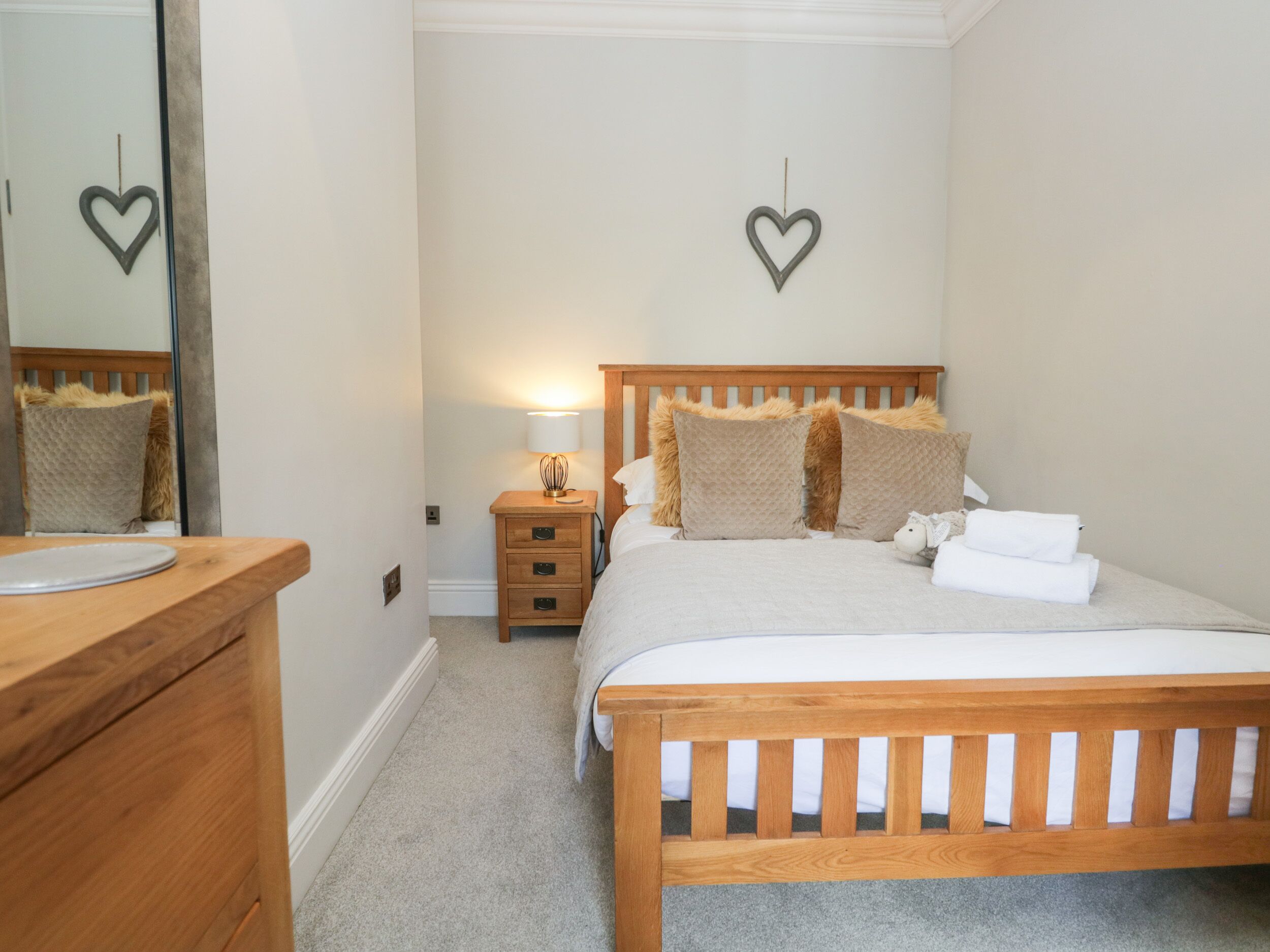 A bedroom with a wooden bed, a bedside table with a lamp, a mirror, and two heart-shaped wall decorations.