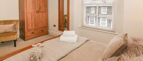 Un dormitorio con cama, armario de madera, espejo y ventana con persianas.