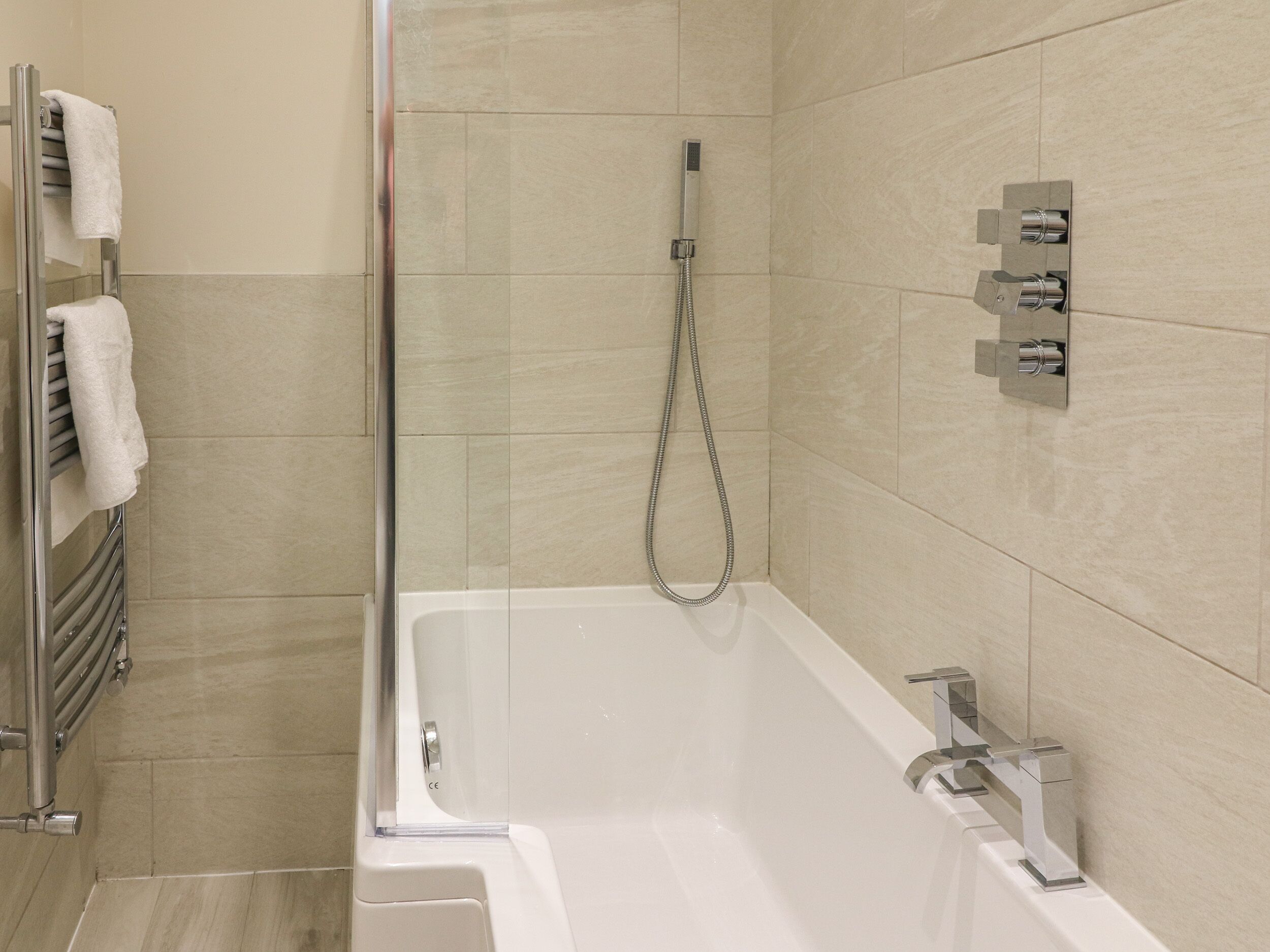 A modern bathroom with a glass-enclosed shower, a white bathtub, and a towel rack with white towels.