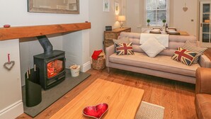 A cozy living room with a fireplace, a sofa with British-themed cushions, and a dining area with a table set for two. - Little Herdwick (Windermere)