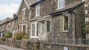 A row of stone houses with traditional architecture, featuring multiple windows and a stone wall with a metal railing. - Little Herdwick (Windermere)