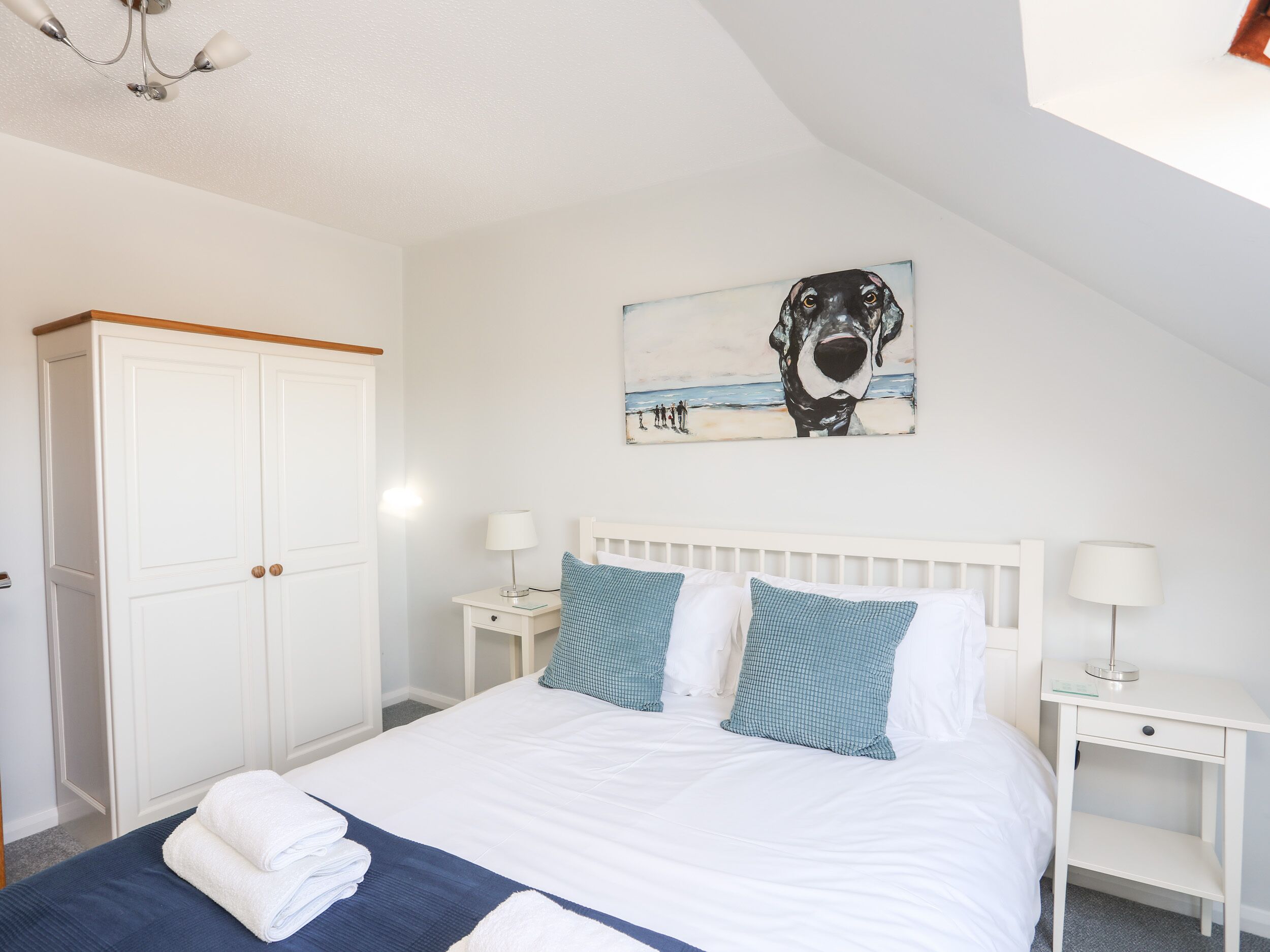 Un dormitorio con cama, mesitas de noche blancas, un armario blanco y una lámpara en el techo.