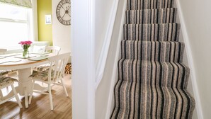A staircase with a striped carpet, a dining area with white chairs and a table, and a wall clock.