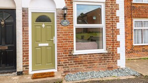 A brick house with a green door, a white window, and a number plaque.