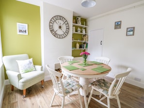 Cozy dining area with a round table and four chairs, a green accent wall, and a large wall clock.