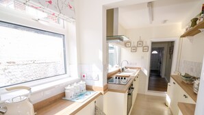 A kitchen with a window, a kettle, a stove, and a sink.