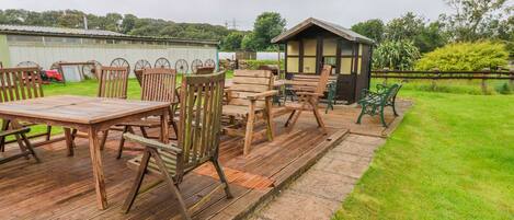 A wooden deck with tables and chairs, a small shed, and a grassy area.