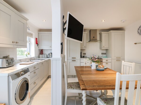 A modern kitchen with white cabinetry, a wooden dining table, and a built-in washing machine. - Offshore (Truro)