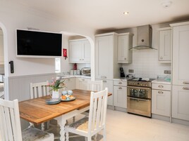 Una cocina moderna con armarios blancos, una mesa de comedor de madera y un televisor de pantalla plana sobre la encimera.