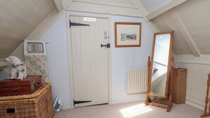 A room with a sloped ceiling, a white door labeled 'PRIVATE,' a framed picture on the wall, a wooden mirror, and a wicker chest of drawers.