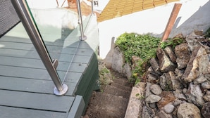 A wooden deck with a metal railing, a stone wall, and a small garden area. - Cobbles House (Whitby)