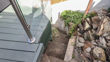A wooden deck with a metal railing, a stone wall, and a small garden area.