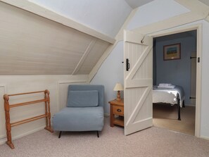 A bedroom with a sloped ceiling, a bed, a nightstand, and a chair.