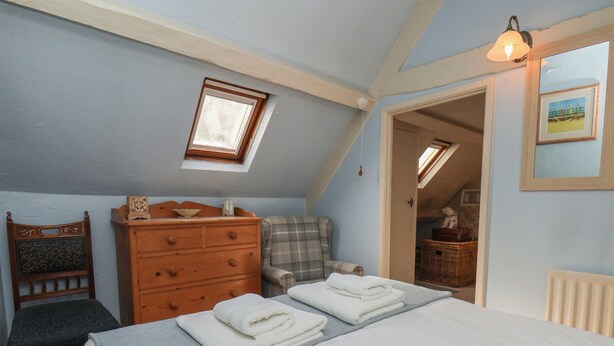 A bedroom with a bed, a dresser, a chair, and a small window.