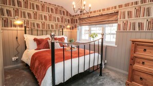 A bedroom with a four-poster bed, a wooden dresser, and bookshelves filled with books. - Esk View Cottage (Whitby)