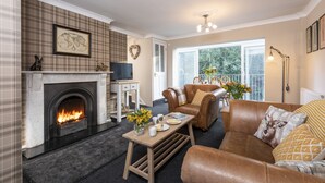 A cozy living room with a fireplace, leather sofa, and a dining area with a table set for two. - Esk View Cottage (Whitby)