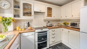 A modern kitchen with white cabinetry, a built-in oven, a dishwasher, and a microwave. - Esk View Cottage (Whitby)