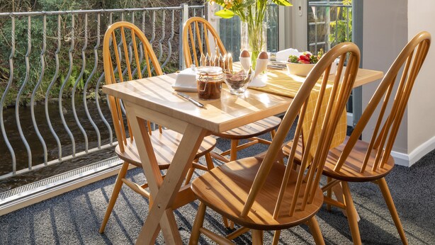 A dining table with chairs, a vase of flowers, and a view of trees through a glass door. - Esk View Cottage (Whitby)