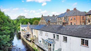 A riverside building with a glass conservatory, a stone facade, and a brick structure with solar panels. - Esk View Cottage (Whitby)