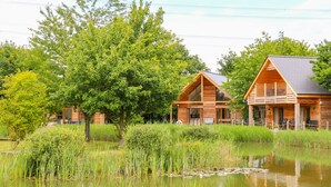 A wooden cabin with a balcony, situated next to a pond with reflections. - Dorado Lodge (Lincoln)
