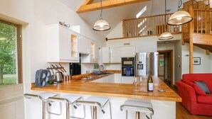 A modern kitchen with a wooden island, stainless steel appliances, and a red sofa in the living area. - Dorado Lodge (Lincoln)