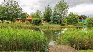 A wooden dock extending into a pond surrounded by lush greenery and trees. - Dorado Lodge (Lincoln)
