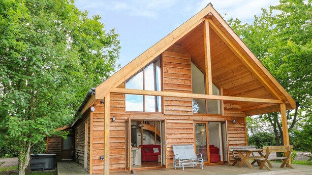 A wooden cabin with a large open porch, a dining table, and a red sofa. - Dorado Lodge (Lincoln)
