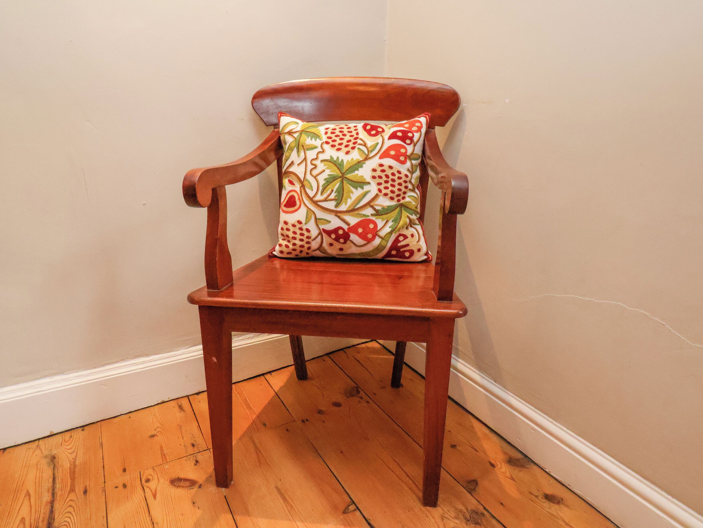 A wooden chair with a floral cushion against a plain wall and wooden flooring.