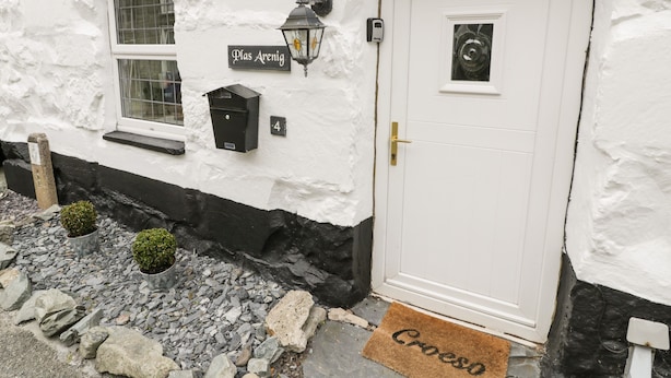 A white building with a black base, a door, a window, a mailbox, and a small lamp. - Plas Arenig (Blaenau Ffestiniog)