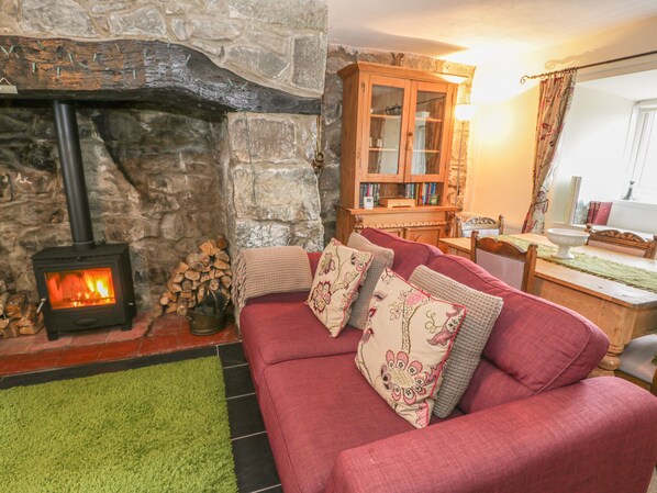 Ein gemütliches Wohnzimmer mit Kamin aus Stein, einem roten Sofa mit Zierkissen, einem Holzkabinett und einem Tisch mit einer Lampe.