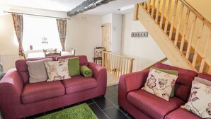 A cozy living room with two red sofas, a green rug, and a wooden staircase. - Plas Arenig (Blaenau Ffestiniog)