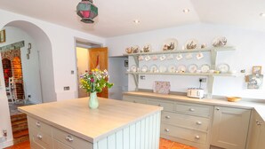 A kitchen with a central island, a brick oven, and a variety of dishes on shelves. - Southrepps Lodge (Norwich)