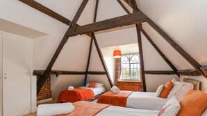 A room with two beds, each with orange bedding and white pillows, under a sloped ceiling with exposed wooden beams. - Southrepps Lodge (Norwich)
