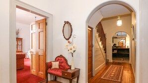 A hallway with wooden flooring, a red upholstered bench, a mirror, and a staircase leading to another room. - Southrepps Lodge (Norwich)