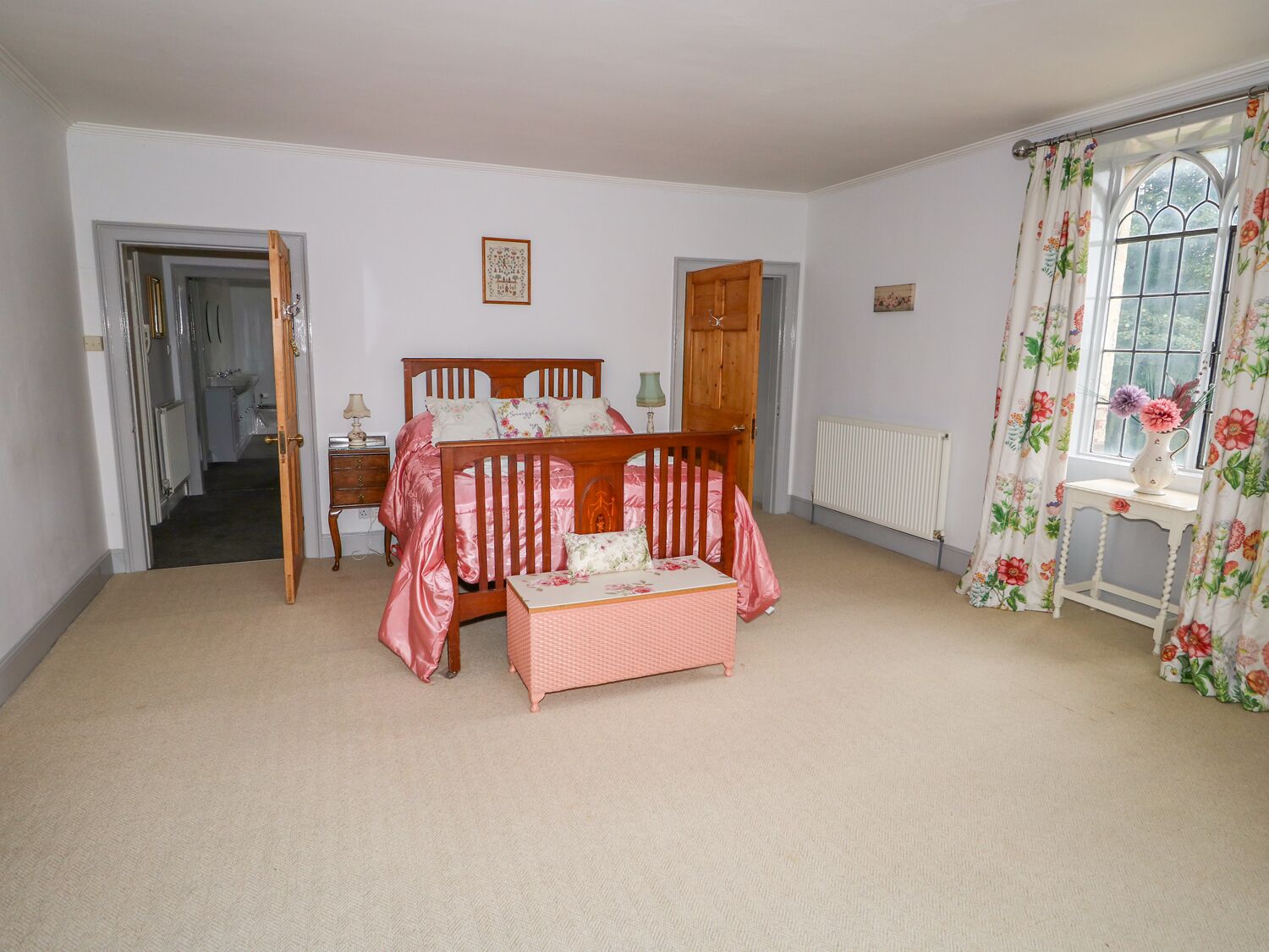 Une chambre à coucher avec un lit à baldaquin, une table de chevet, une commode et une fenêtre ornée de rideaux à motifs floraux.