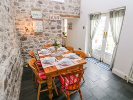 Un comedor con pared de piedra, una mesa de madera dispuesta para cuatro personas y vistas al exterior a través de una puerta con cortinas.
