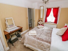 A bedroom with a bed, a sewing machine, a mirror, and a window with red curtains.