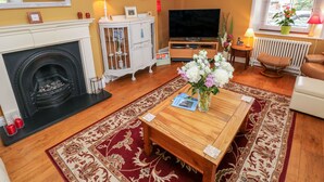 A living room with a fireplace, TV, and a coffee table with a vase of flowers. - Castle School House (Kidwelly)