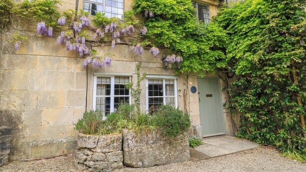A stone building with a traditional design, featuring a door, windows, and a small garden area with plants and a gravel path. - October Cottage (Stroud)