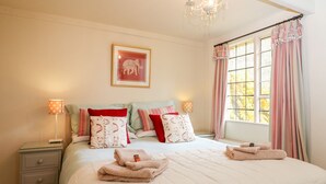 A neatly made bed with a quilt, pillows, and folded towels. There is a nightstand with a lamp and a framed picture on the wall. - October Cottage (Stroud)