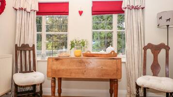 A cozy room with a wooden table, two chairs, a radiator, and two windows with red curtains.