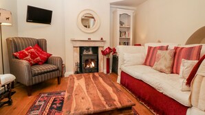 A living room with a fireplace, a sofa, a chair, and a coffee table. - October Cottage (Stroud)