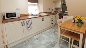 A compact kitchen with white cabinets, a microwave, a sink, and a dining area with a table and chairs.