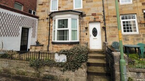 A traditional stone house with a bay window, a white door, and a small garden area with a sign.